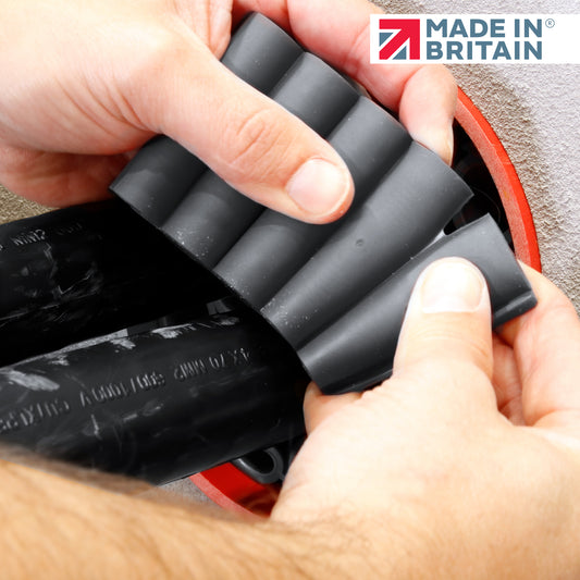 Hands applying grey fire-rated duct sealant around electrical cables during installation, showing flexible material placement. Made in Britain logo visible.