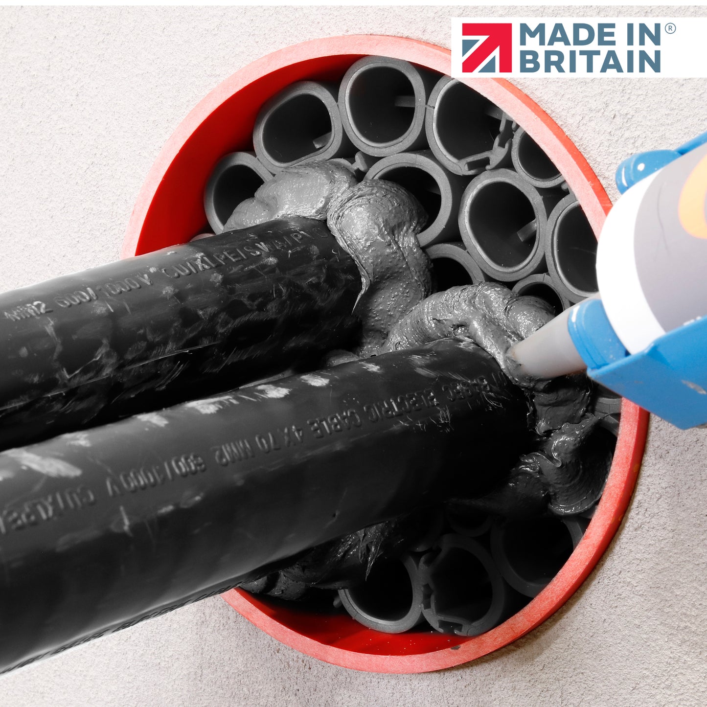 Application of DuctSeal FR fire-resistant sealant around black cable ducts inside a red-sealed opening, using a caulking gun, with the ‘Made in Britain’ logo displayed.