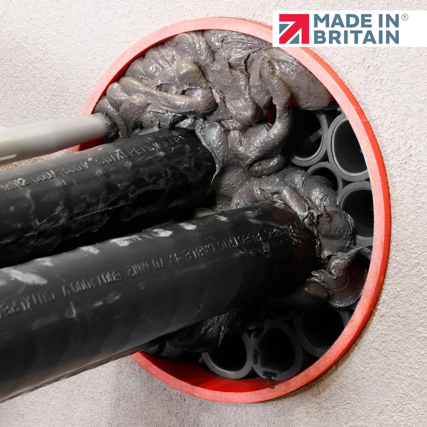 Close-up of DuctSeal FR fire-rated sealant applied around black cable ducts within a red-sealed circular wall opening, showing dense grey fireproof sealant and the ‘Made in Britain’ logo.