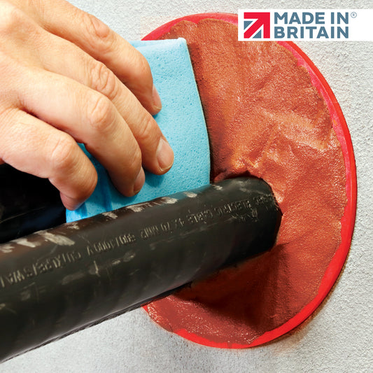 Hand finishing cured DuctSeal RedStuff around a black cable duct with a blue sanding pad; sealed wall penetration with Made in Britain logo visible