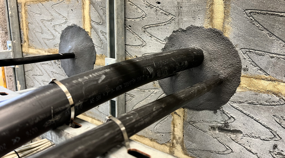 Close-up of multiple electrical cables sealed with duct seal compound inside a concrete wall, showing a watertight installation in an industrial setting.