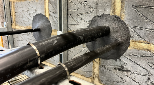 Close-up of multiple electrical cables sealed with duct seal compound inside a concrete wall, showing a watertight installation in an industrial setting.